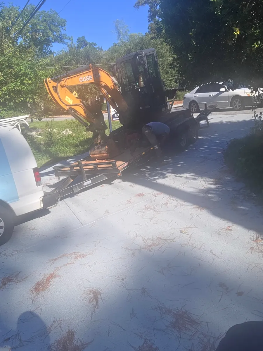 Compact excavator being unloaded from a trailer at a residential driveway