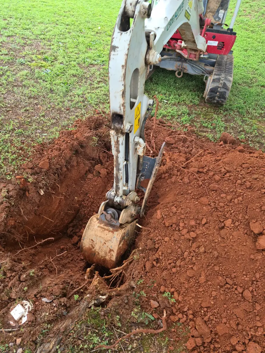 Mini excavator digging a trench in a grassy yard to reach a buried pipe